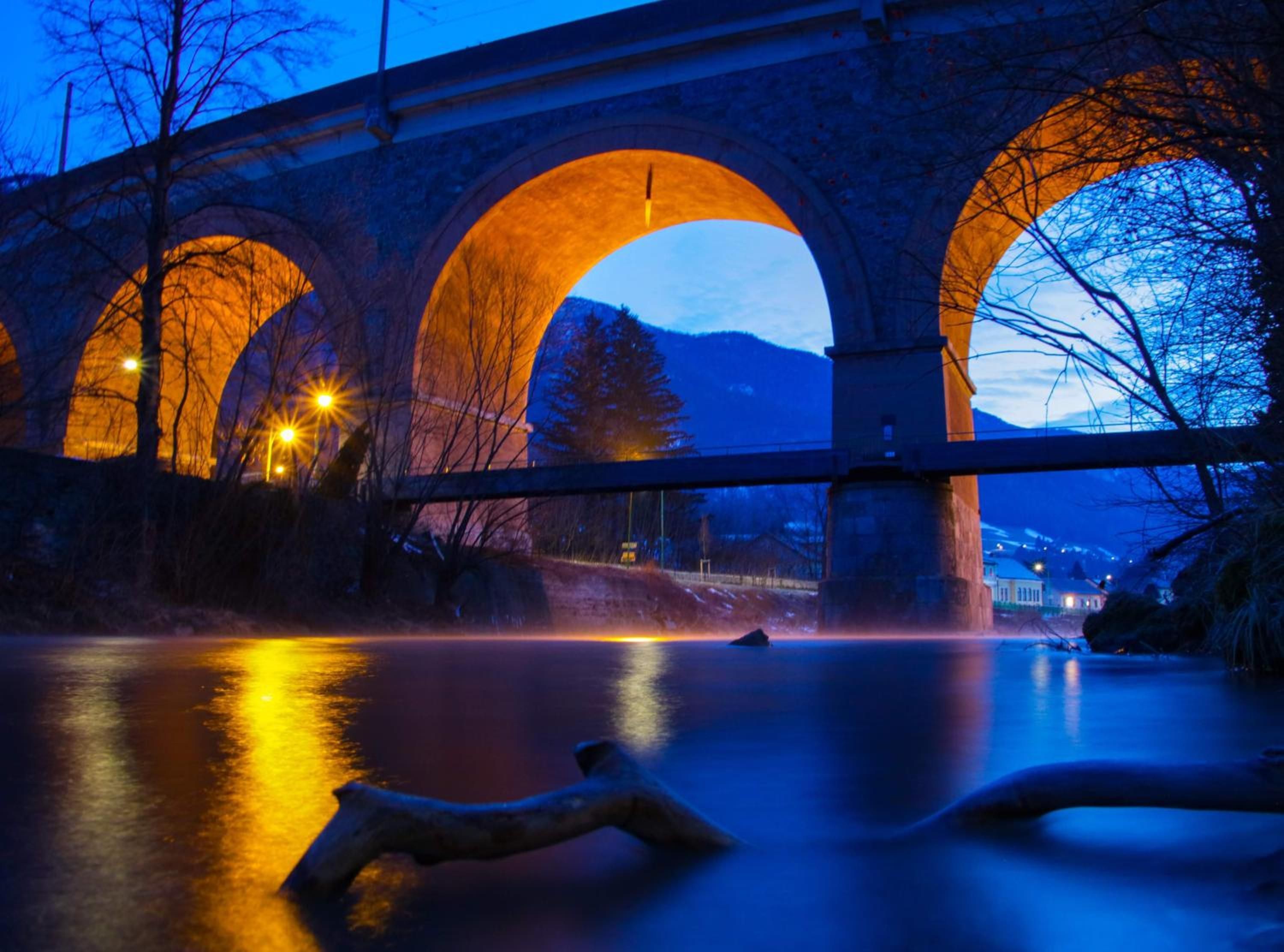 A stone bridge with three arches over a body of water, illuminated by streetlights.