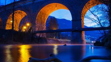 A stone bridge with three arches over a body of water, illuminated by streetlights.