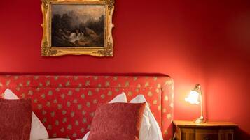 Ein Hotelzimmer mit roter Wand, einem gerahmten Gemälde, einem Bett mit roter und weißer Bettwäsche und einem Nachttisch mit einer Lampe.