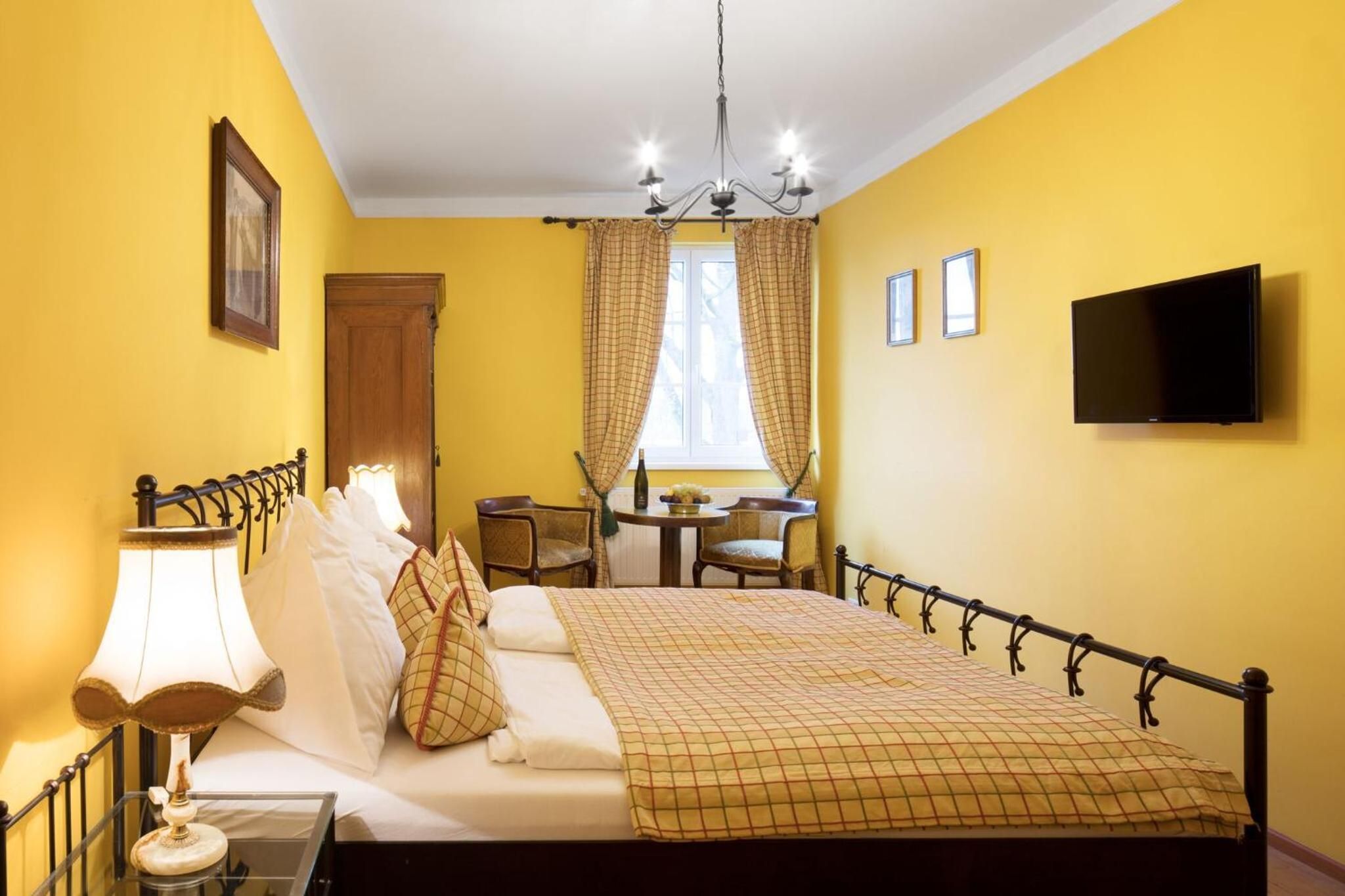 A hotel room with a bed, bedside lamp, curtains, a desk with a chair, a television, and a window.