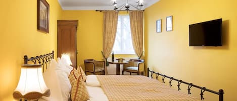Une chambre d’hôtel comprenant un lit, une lampe de chevet, des rideaux, un bureau avec une chaise, une télévision et une fenêtre.