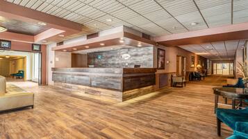 A hotel lobby with a reception desk, wooden flooring, and a modern ceiling design.