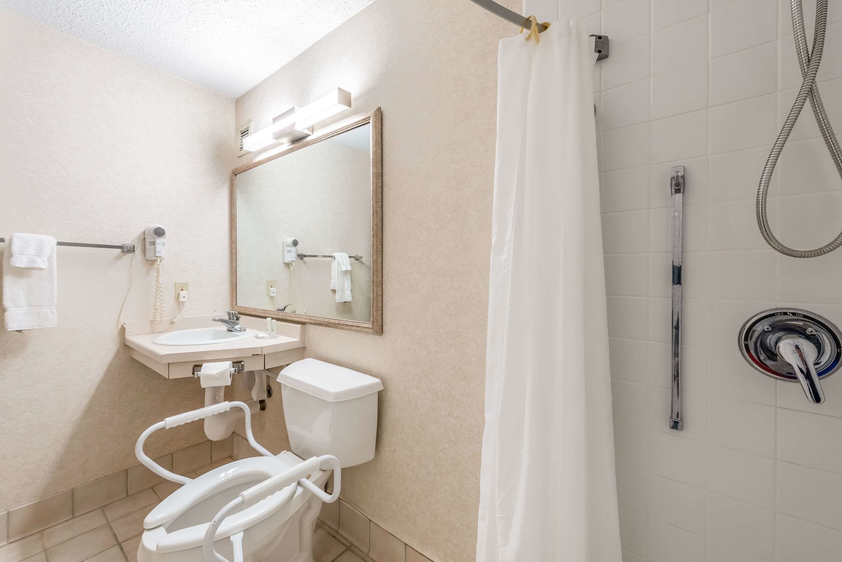 A bathroom with a toilet, sink, mirror, and shower.