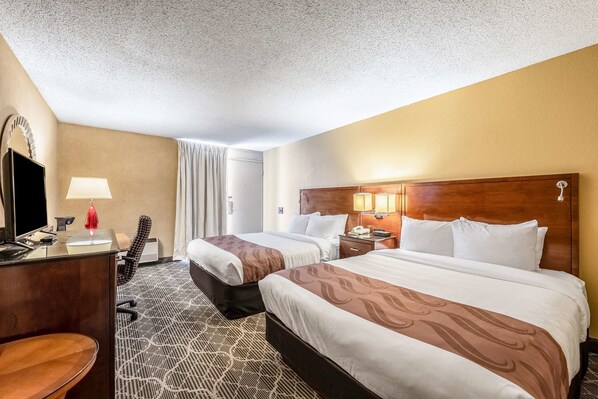 A hotel room with two beds, a desk with a lamp, a chair, and a TV. - Quality Inn & Suites Brainerd (Brainerd)