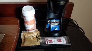 A coffee maker, a stack of disposable coffee cups, a bag of coffee pods, and a tray with sugar packets on a countertop.