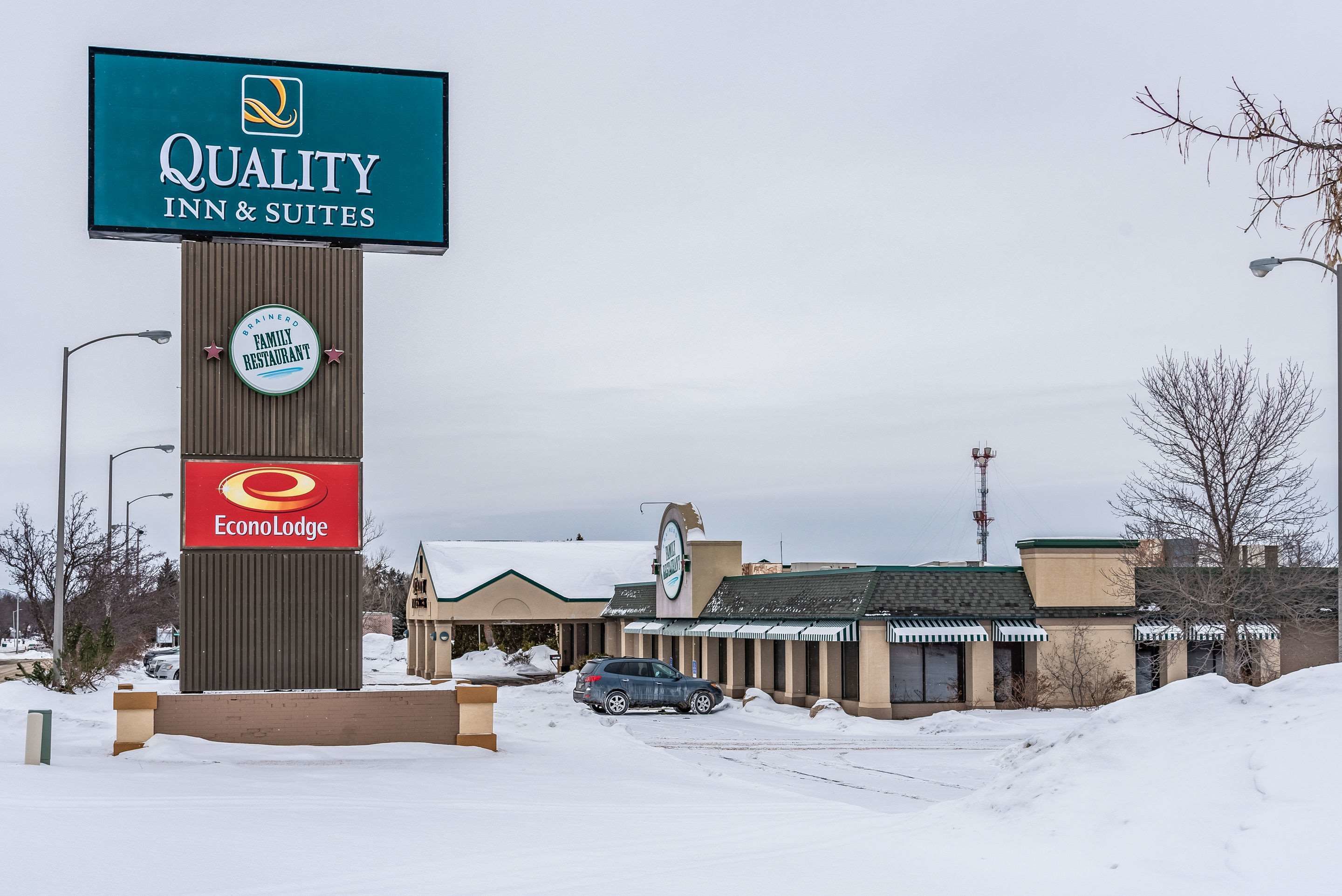 Señalización de Quality Inn & Suites, un letrero de restaurante familiar y una señal de EconoLodge en un estacionamiento nevado.