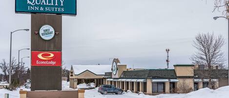 Señalización de Quality Inn & Suites, un letrero de restaurante familiar y una señal de EconoLodge en un estacionamiento nevado.