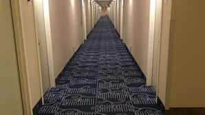 Pasillo de hotel con alfombra estampada, suelo de madera y puertas a ambos lados.