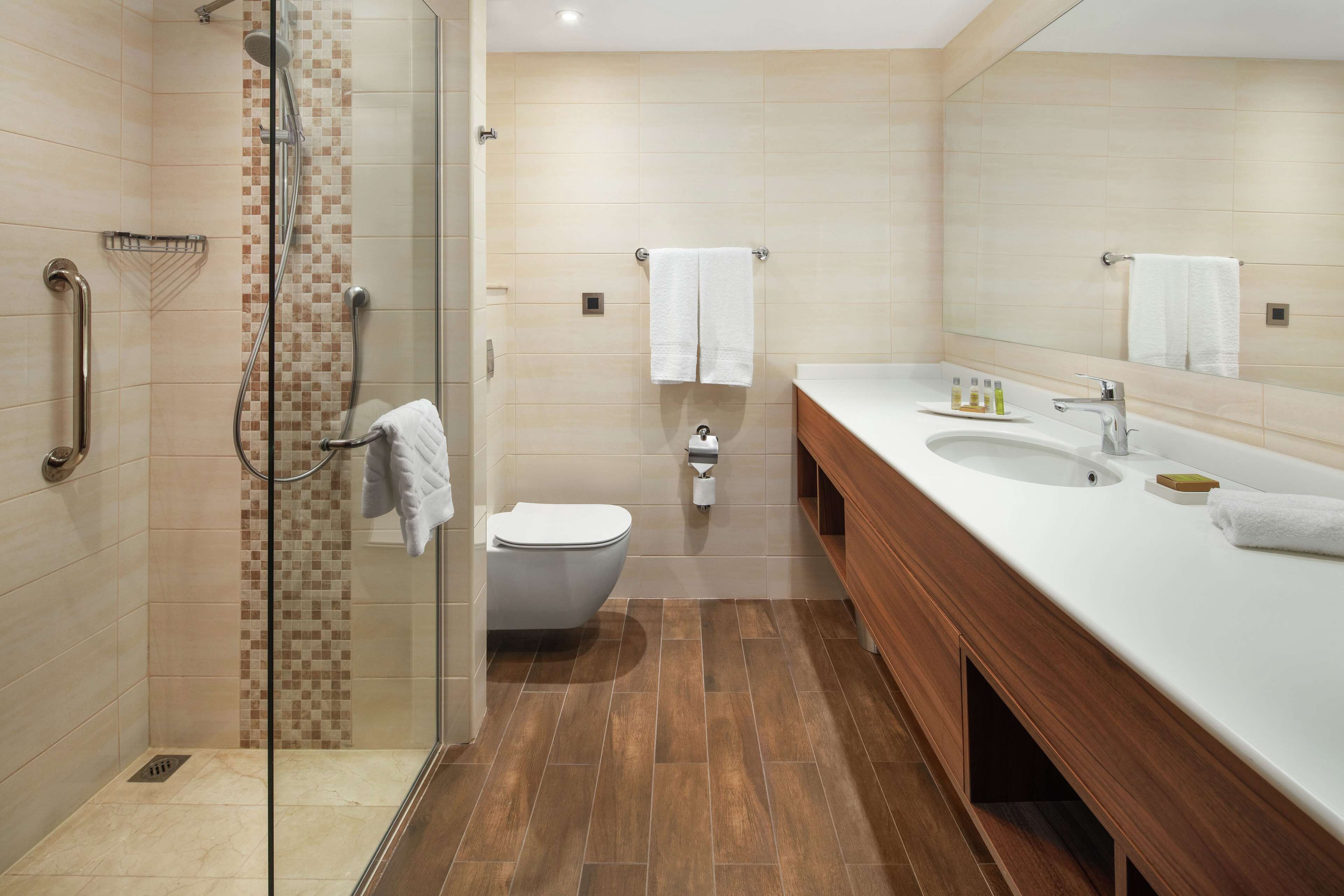 Een moderne badkamer met een douchecabine van glas, een apart toilet en een wastafel met een wasbak en spiegel.