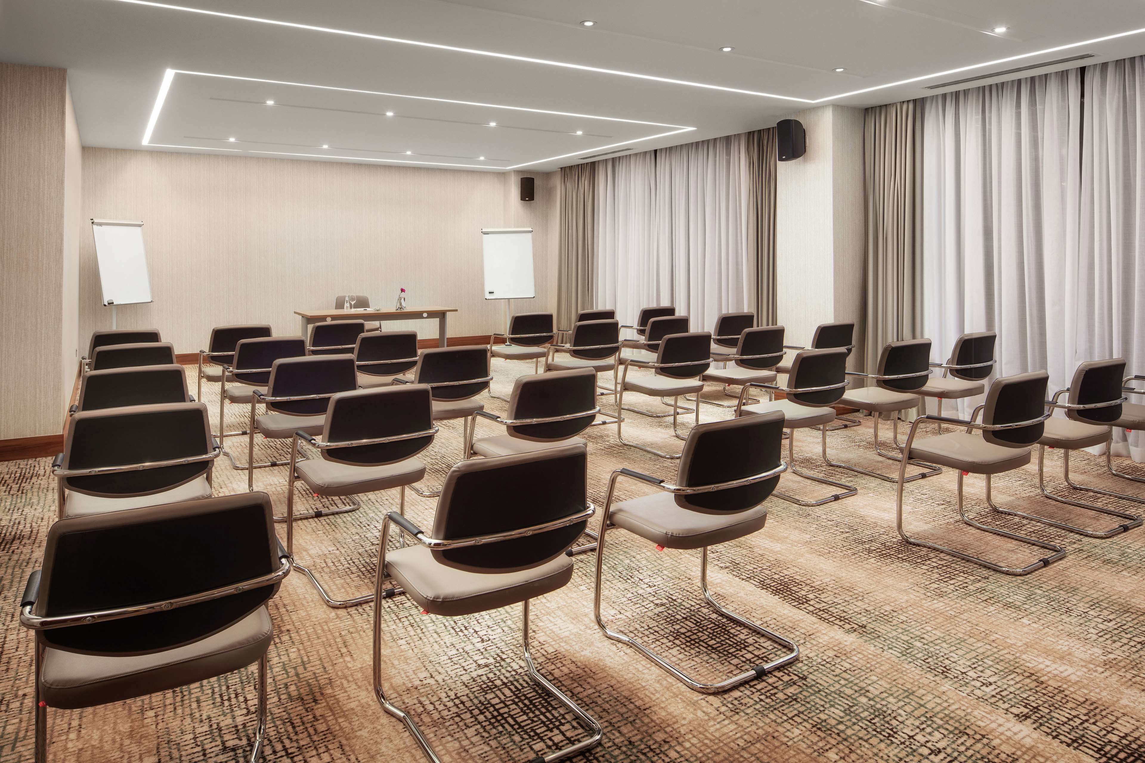 Ein Konferenzraum mit Reihen von Stühlen, einer Tafel und einer Projektionsleinwand.