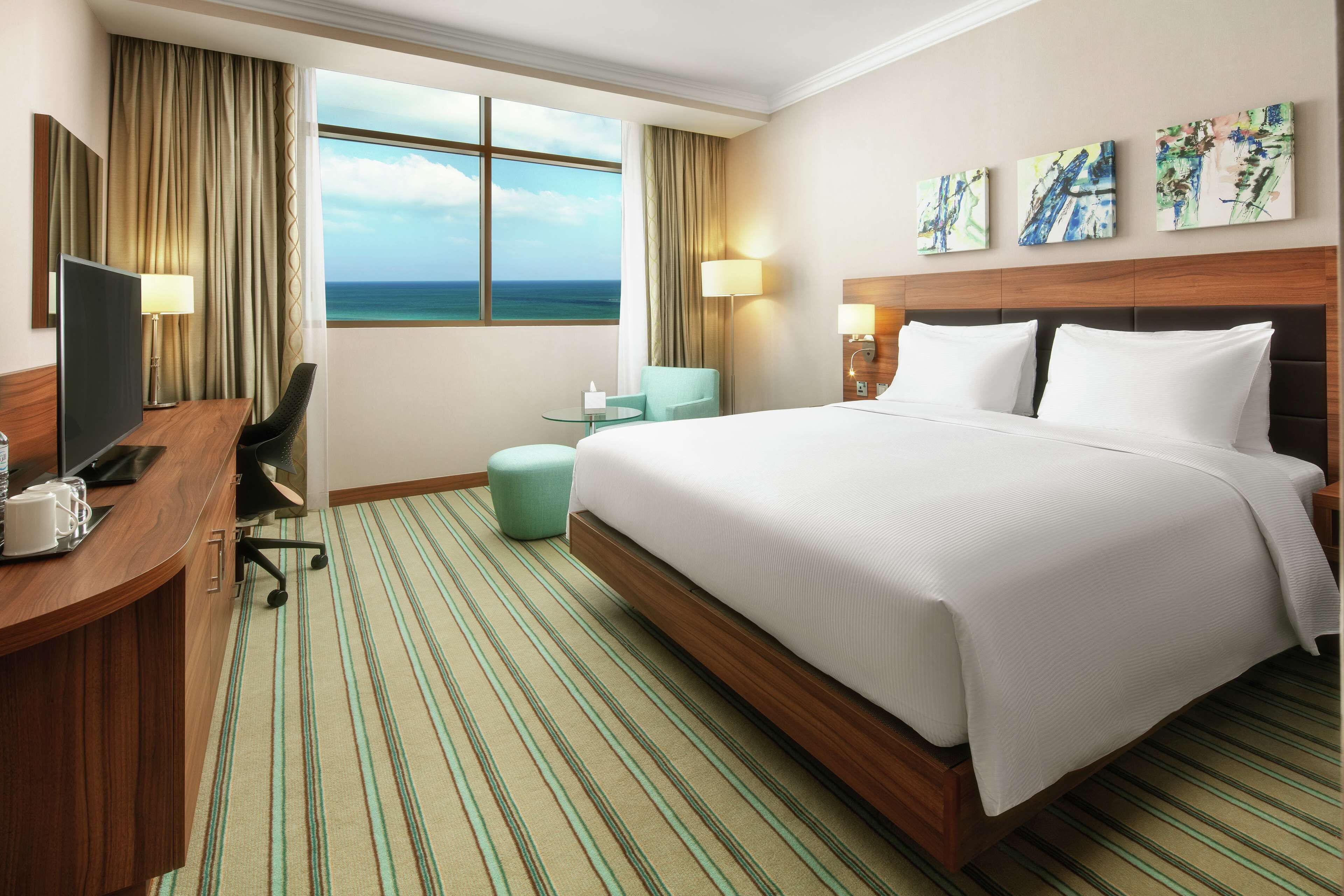 Habitación de hotel con una cama grande, un escritorio con computadora, una silla y vista al océano.