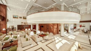 Eine großzügige Lobby mit einer zentralen, runden Sitzecke, einer hohen Decke mit aufwendigen Mustern und einem Balkon mit Blick auf den Raum.