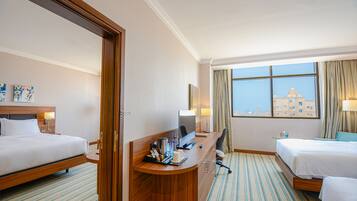 Ein Hotelzimmer mit zwei Betten, einem Schreibtisch mit Computer, einem Stuhl und Blick auf ein Gebäude durch das Fenster.