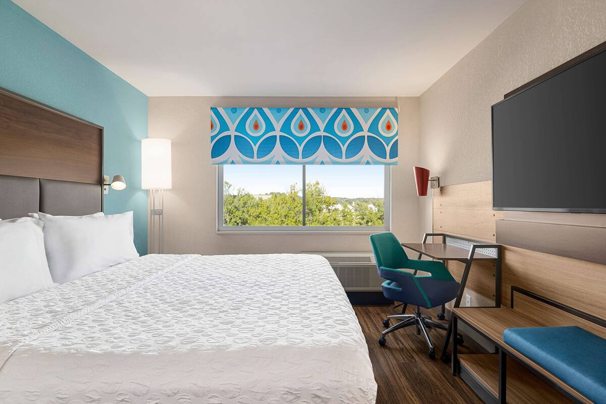Une chambre d’hôtel équipée d’un lit, d’un bureau, d’une chaise, d’une grande fenêtre avec vue et d’un téléviseur.