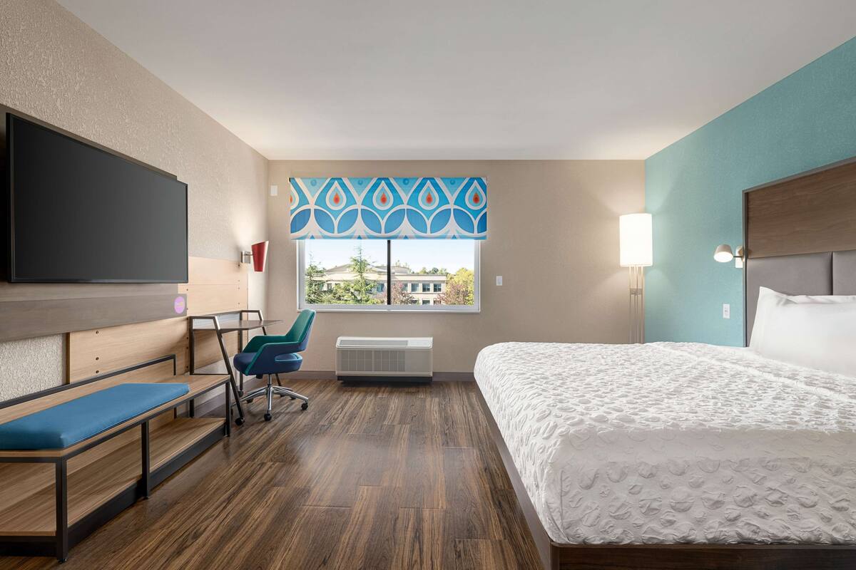 Une chambre d’hôtel comprenant un lit, un bureau avec une chaise, une télévision, une fenêtre avec vue et un rideau à motifs.