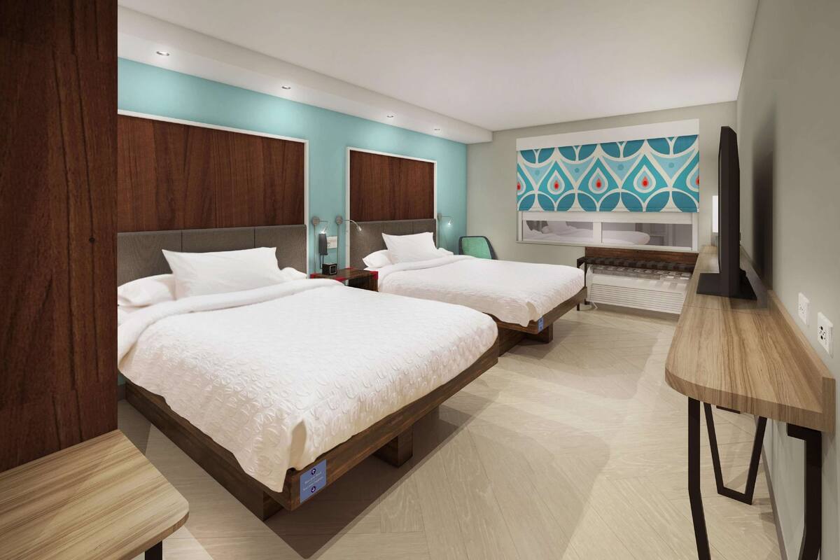 Une chambre d’hôtel avec deux lits, un bureau, une télévision et une salle de bain avec douche et toilettes.