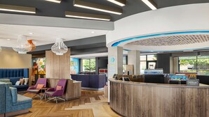 A modern hotel lobby with a reception desk, seating area, and a mural on the wall.