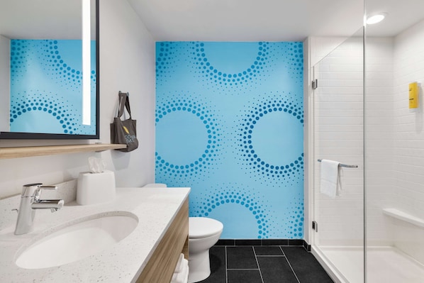 A modern bathroom with a white sink, toilet, and shower. The wall features a blue dotted pattern.