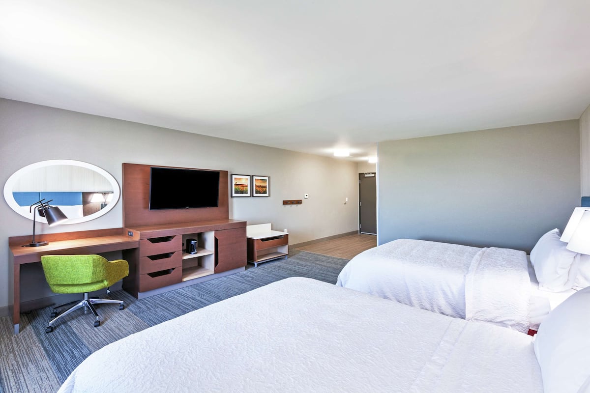 A hotel room with two beds, a desk with a chair, a television, and a mirror.