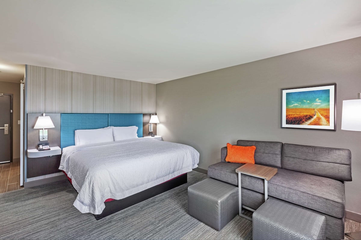 A hotel room with a bed, a sofa, a nightstand, and a painting on the wall.