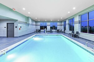 Una piscina interior moderna con agua cristalina, rodeada de sillones de descanso y un muro de vidrio.