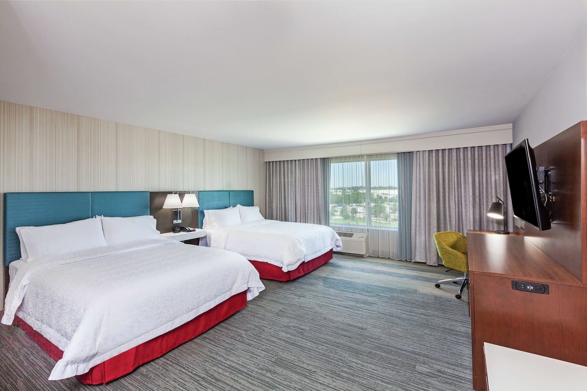 A hotel room with two beds, a desk, a chair, a TV, and a window with curtains.