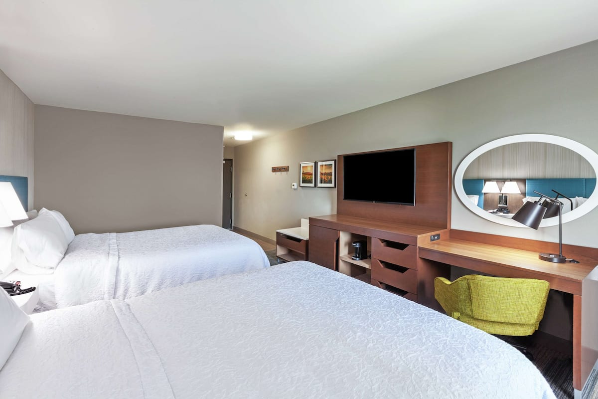 A hotel room with two beds, a desk with a chair, a TV, and a mirror.