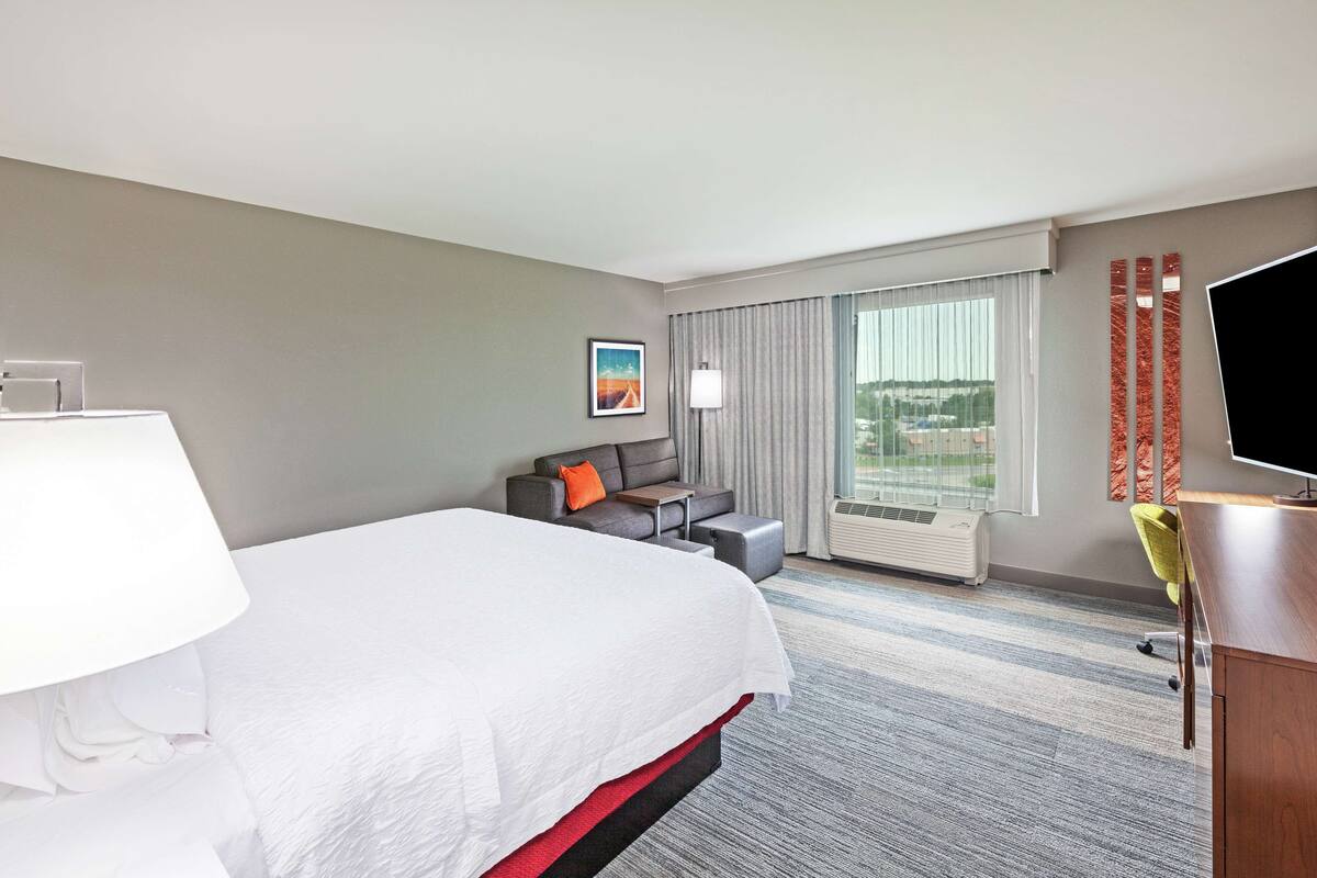 A hotel room with a large bed, a desk, a chair, a sofa, and a TV.