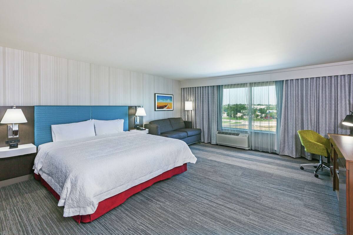A hotel room with a large bed, a sofa, a desk, and a view of the outdoors.