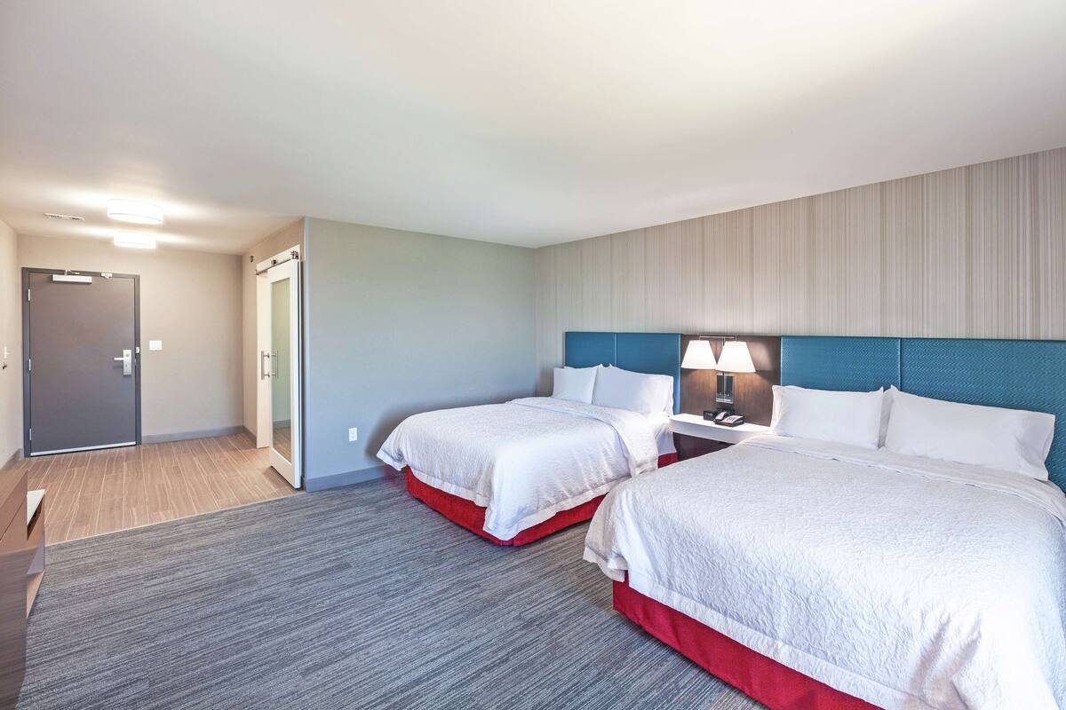 A hotel room with two beds, a desk, and a door.
