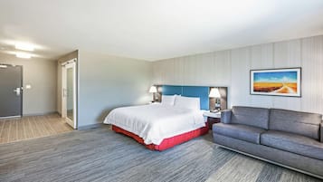 A hotel room with a bed, a sofa, a painting on the wall, and a door.