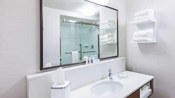 A modern bathroom with a large mirror, a sink, and a glass shower enclosure.