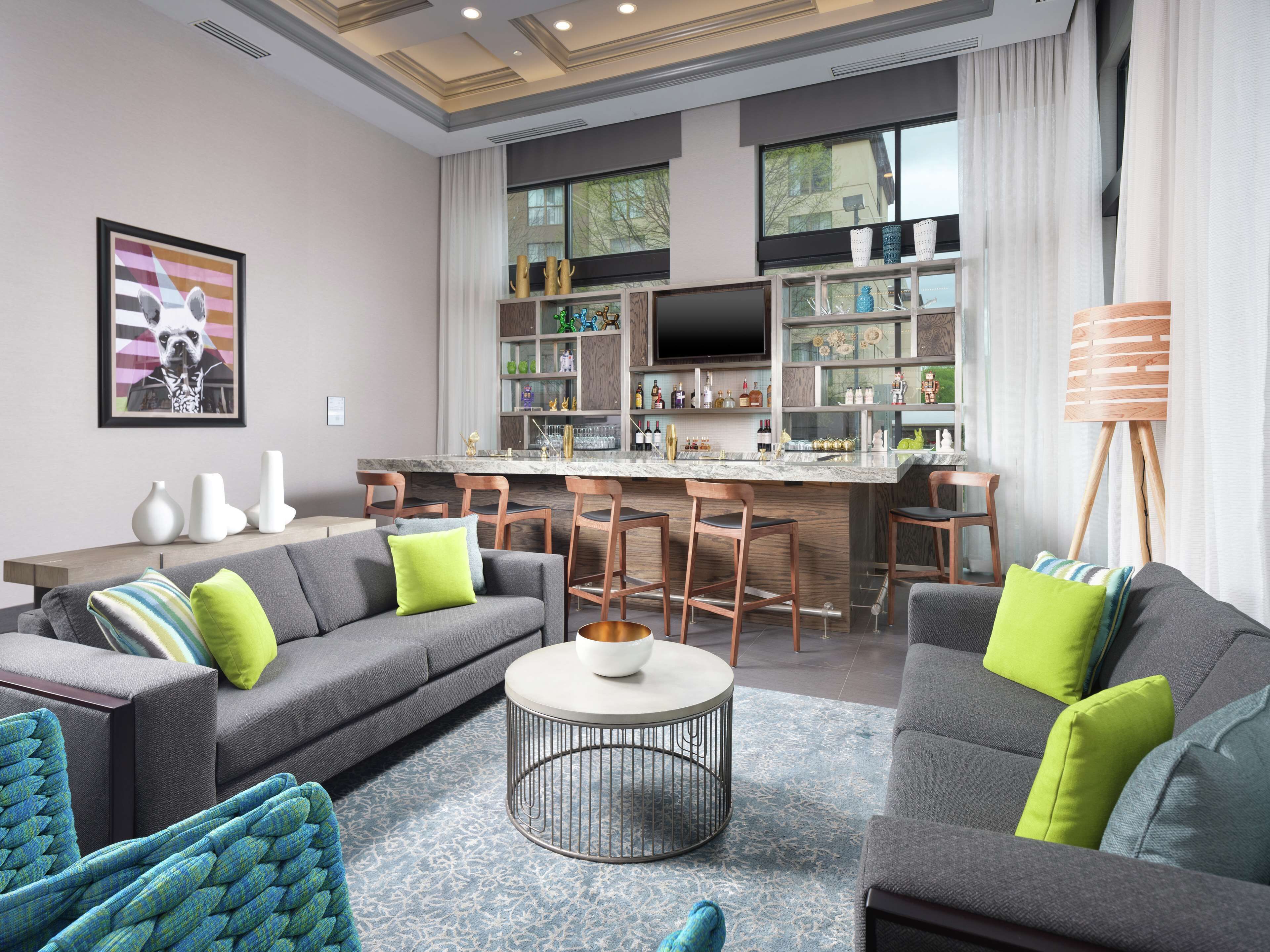 A modern living room with a grey sofa, green cushions, a round coffee table, and a kitchen area with a bar and bar stools.