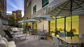 An outdoor patio area with wicker furniture and striped umbrellas, overlooking a building with large windows. - Hampton Inn & Suites Atlanta Decatur/Emory (Decatur)