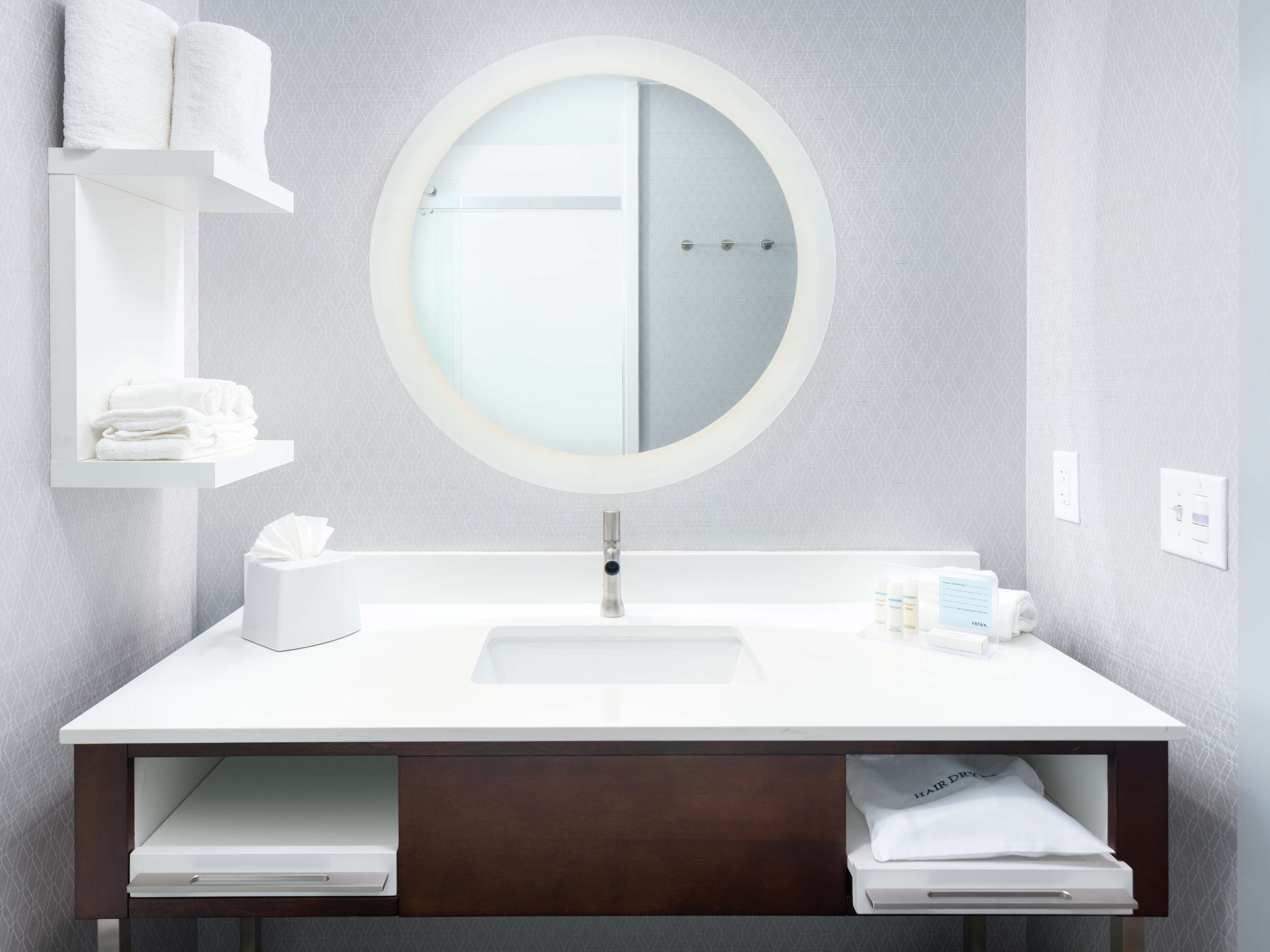 A modern bathroom with a round mirror, white sink, and towel storage.
