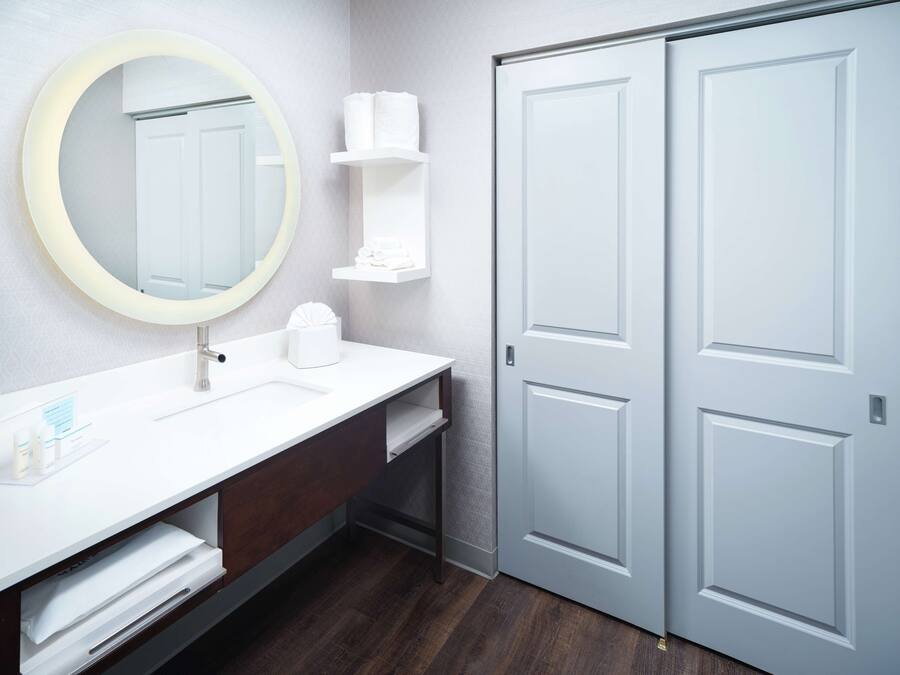 A modern bathroom with a round mirror, white sink, and two white doors.