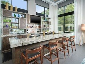 A modern kitchen with a marble countertop, wooden bar stools, and a large window offering a view of the outdoors.