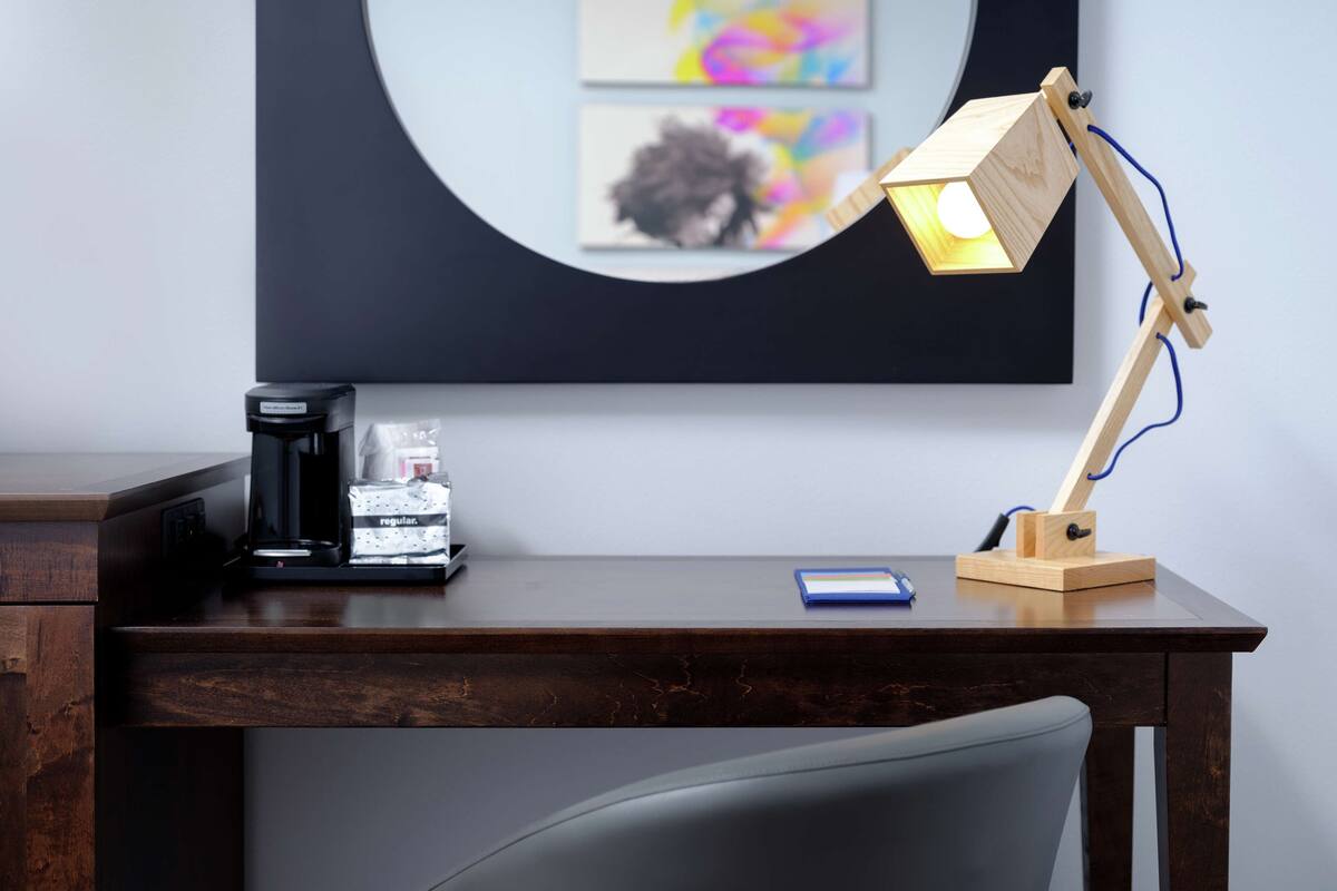 A wooden desk with a coffee maker, a smartphone, and a wooden desk lamp.