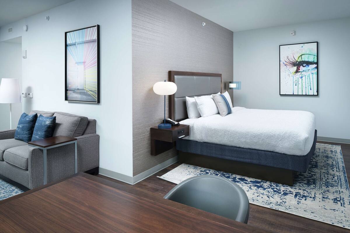 A modern hotel room with a bed, a desk, a chair, and artwork on the walls.