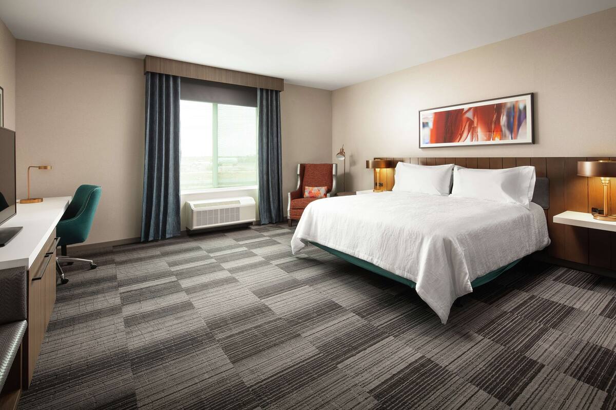 A hotel room with a large bed, a desk, a chair, and a window with curtains.