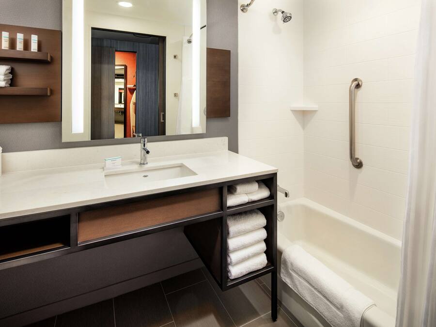 Un baño moderno con lavamanos blanco, tocador de madera oscura y cabina de ducha con mampara de vidrio.
