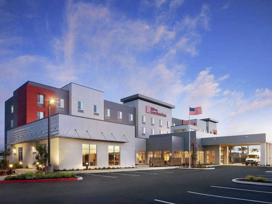 A modern hotel with a flat roof, large windows, and a parking lot.