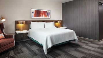Habitación de hotel con cama, dos mesitas de noche con lámparas, una silla y un cuadro abstracto grande en la pared.