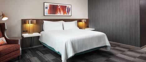 A hotel room with a bed, two bedside tables with lamps, a chair, and a large abstract painting on the wall.