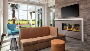 Un salon moderne avec un canapé, un pouf et une petite table. On aperçoit une cheminée sur le mur, et un téléviseur est fixé au-dessus.