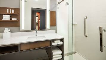 Une salle de bain moderne avec un lavabo blanc, un grand miroir et une cabine de douche en verre.