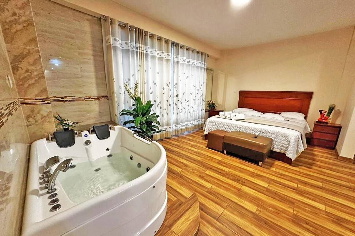 A hotel room with a large bathtub, a bed with a wooden headboard, and a wooden floor.