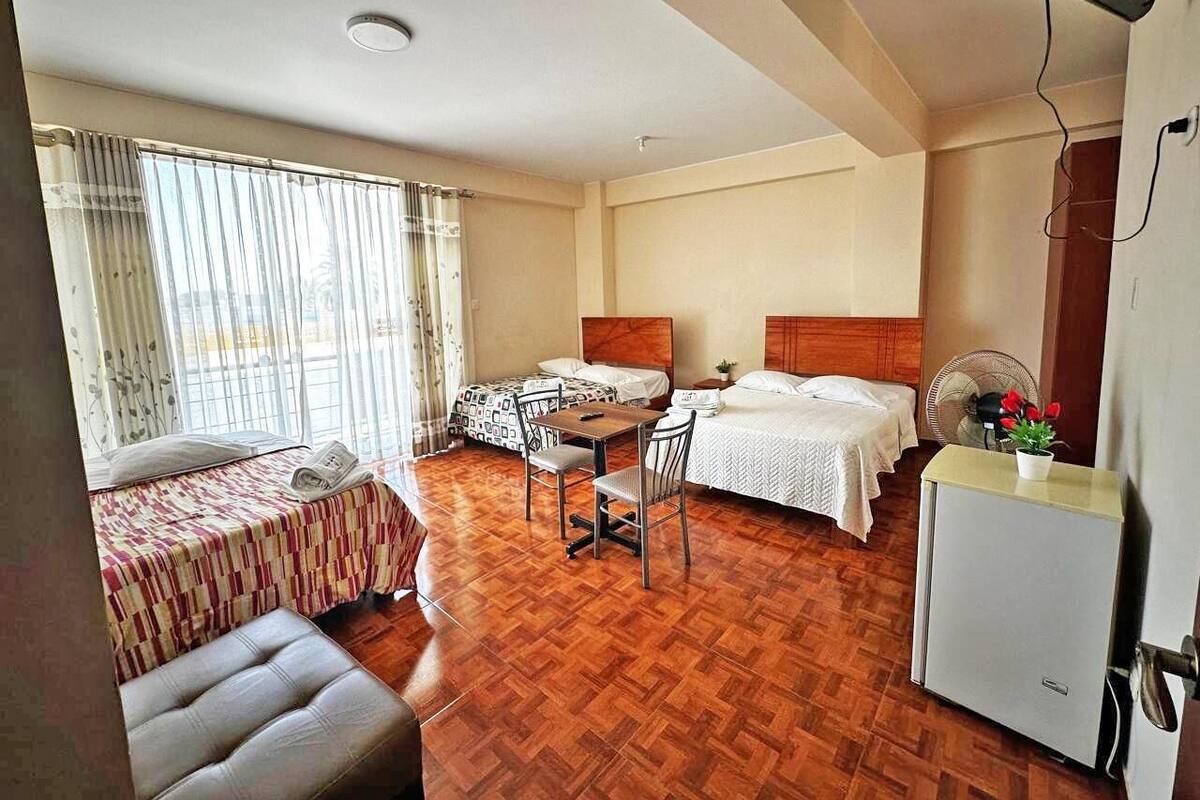A hotel room with two beds, a dining table, a small refrigerator, and a window with curtains.