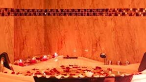 Eine Badewanne mit Rosenblättern und Kerzen, die eine romantische Atmosphäre vermittelt.