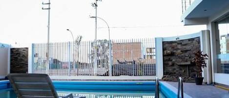 An outdoor swimming pool area with a bench, a fence, and a stone wall.